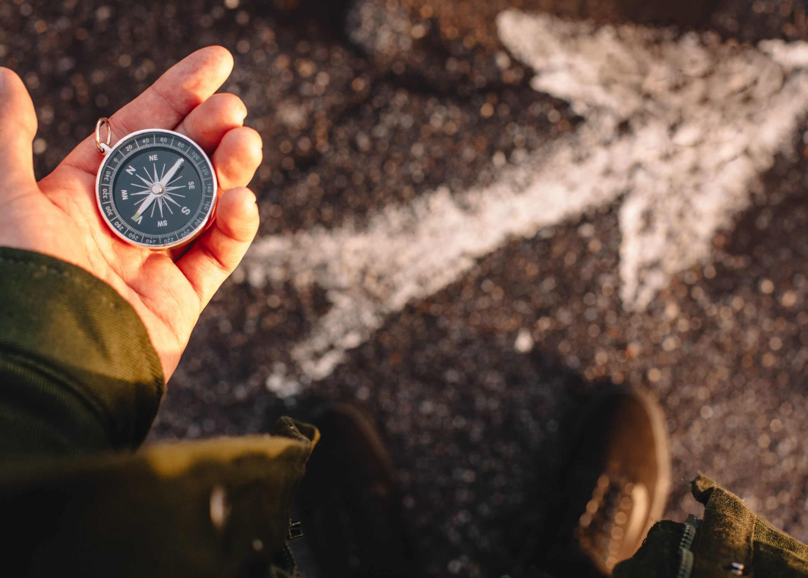 hand holding a compass, with an arrow on the pavement