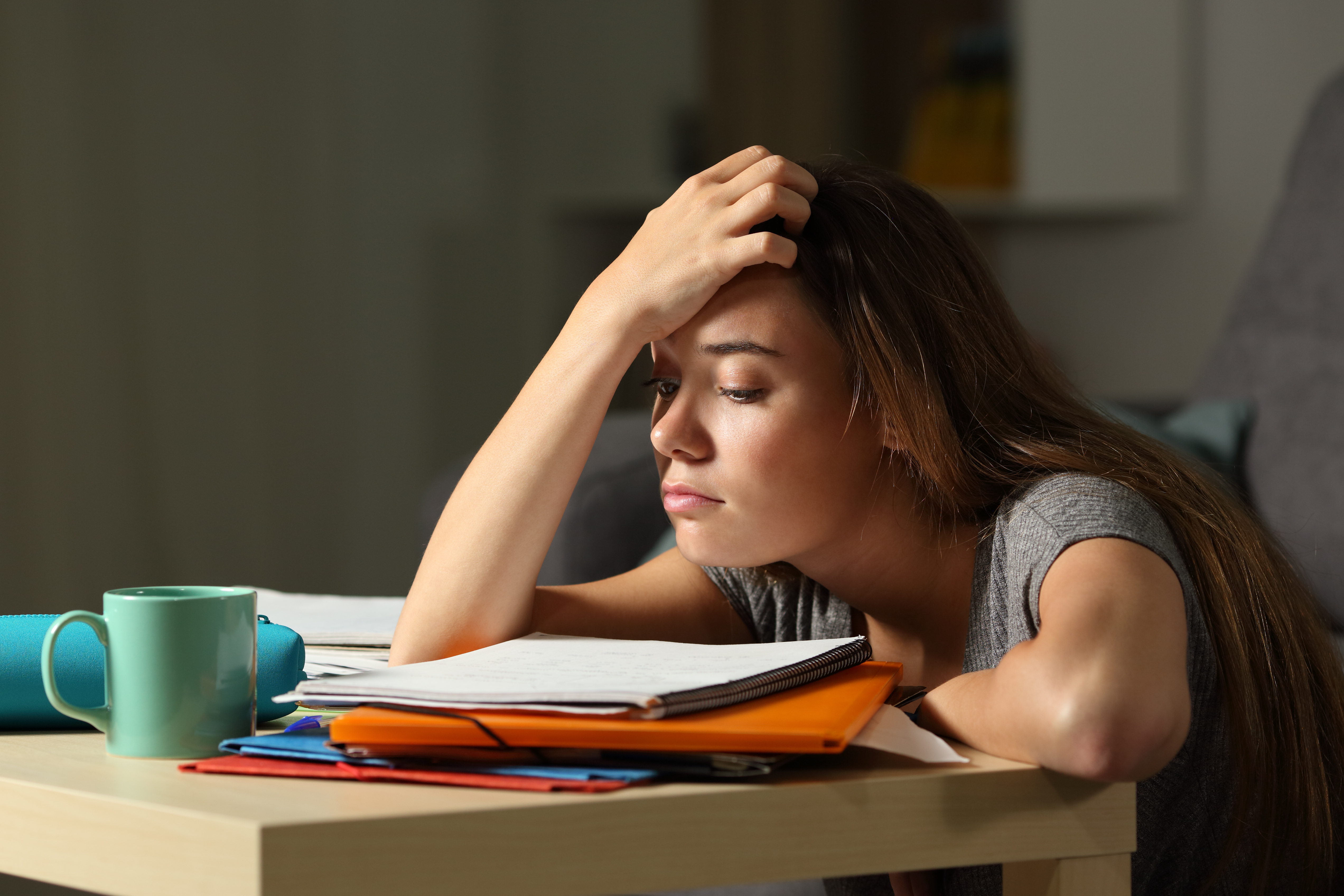 A student sitting at a desk hunched over books appearing stressed.