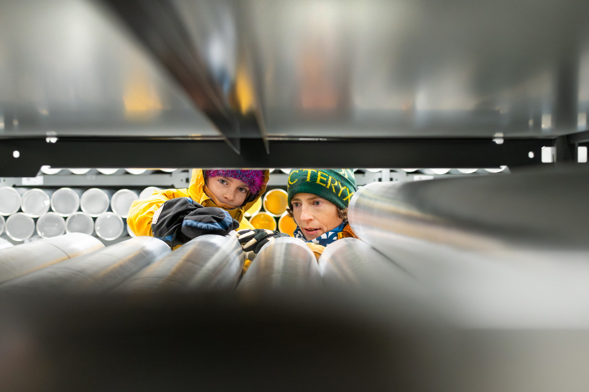 Alison Criscitiello, U of A glaciologist and recipient of the 2025 Summit of Excellence award, examines ice cores in the Canadian Ice Core Lab alongside her daughter, Winter. The pair peek through the shelves, examining labels on metal tubes containing ice core samples.